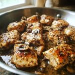 Close-up of pieces of Garlic Butter Chicken and Mushroom Skillet Dinner simmering in a rich, herbed sauce in a stainless steel pan.