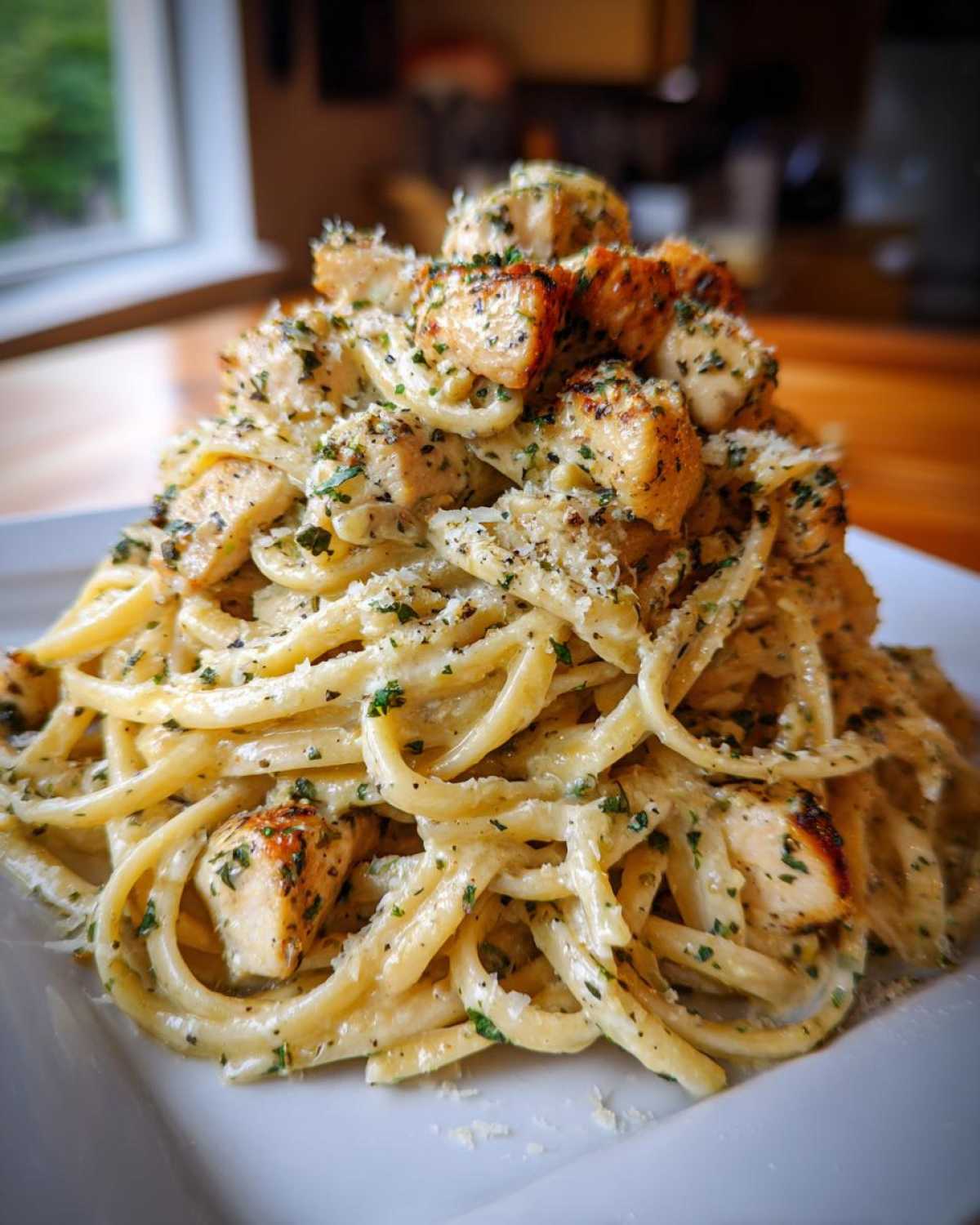 A tall mound of creamy Garlic Butter Chicken Pasta with Parmesan, topped with seasoned chicken pieces and fresh parsley.