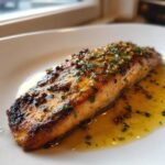 A perfectly cooked fillet of Garlic Butter Salmon with crispy edges resting in a pool of melted butter sauce.