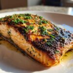 A perfectly cooked fillet of Garlic Butter Salmon with crispy skin, topped with fresh parsley and resting in butter sauce.