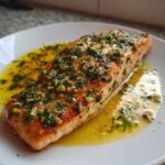 A perfectly cooked fillet of Garlic Butter Salmon with Lemon Herb Sauce resting in a pool of melted butter and herbs.
