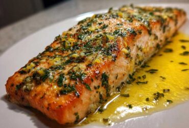 A perfectly cooked fillet of Garlic Butter Salmon with Lemon Herb Sauce glistening on a white plate.
