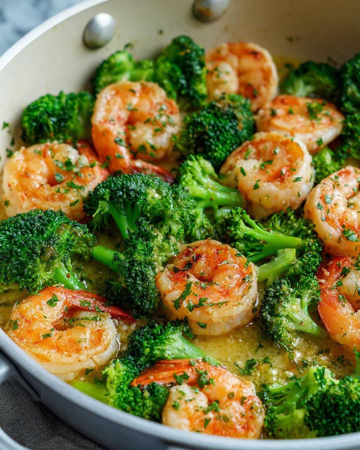 Close-up of plump shrimp and bright green broccoli florets simmering in garlic butter sauce.