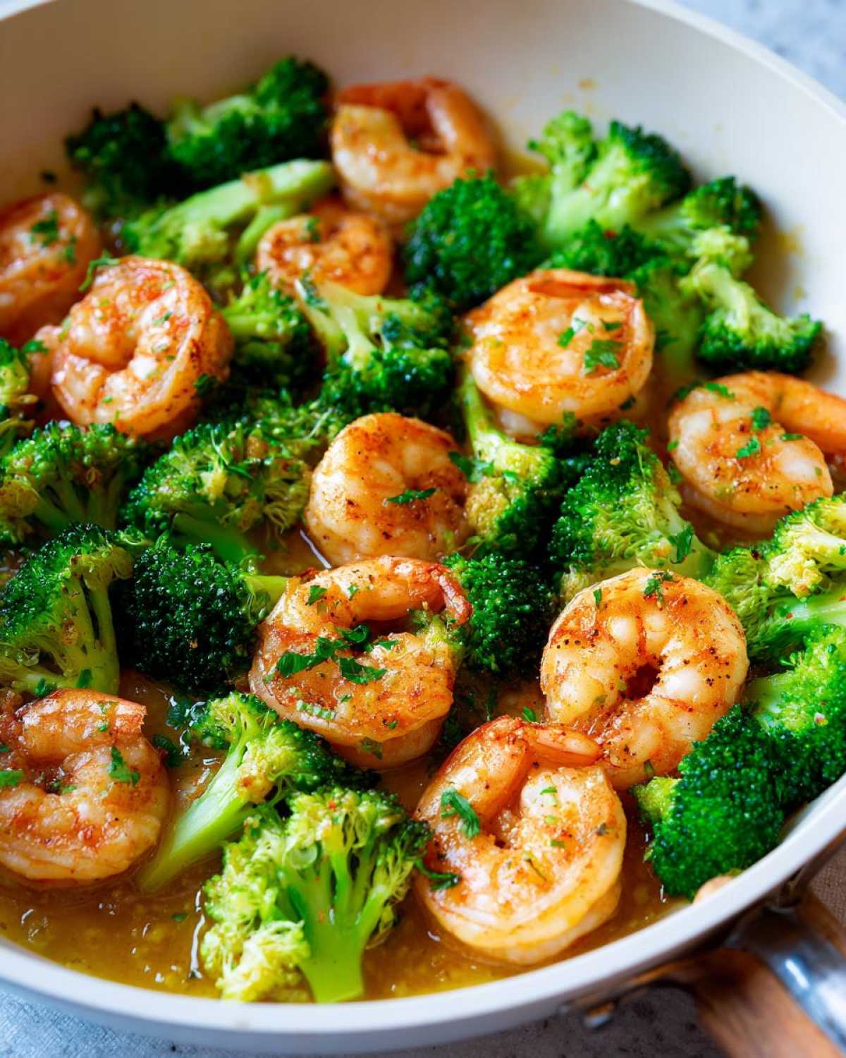 Close-up of plump, seasoned shrimp and bright green broccoli florets simmering in garlic butter sauce in a skillet.
