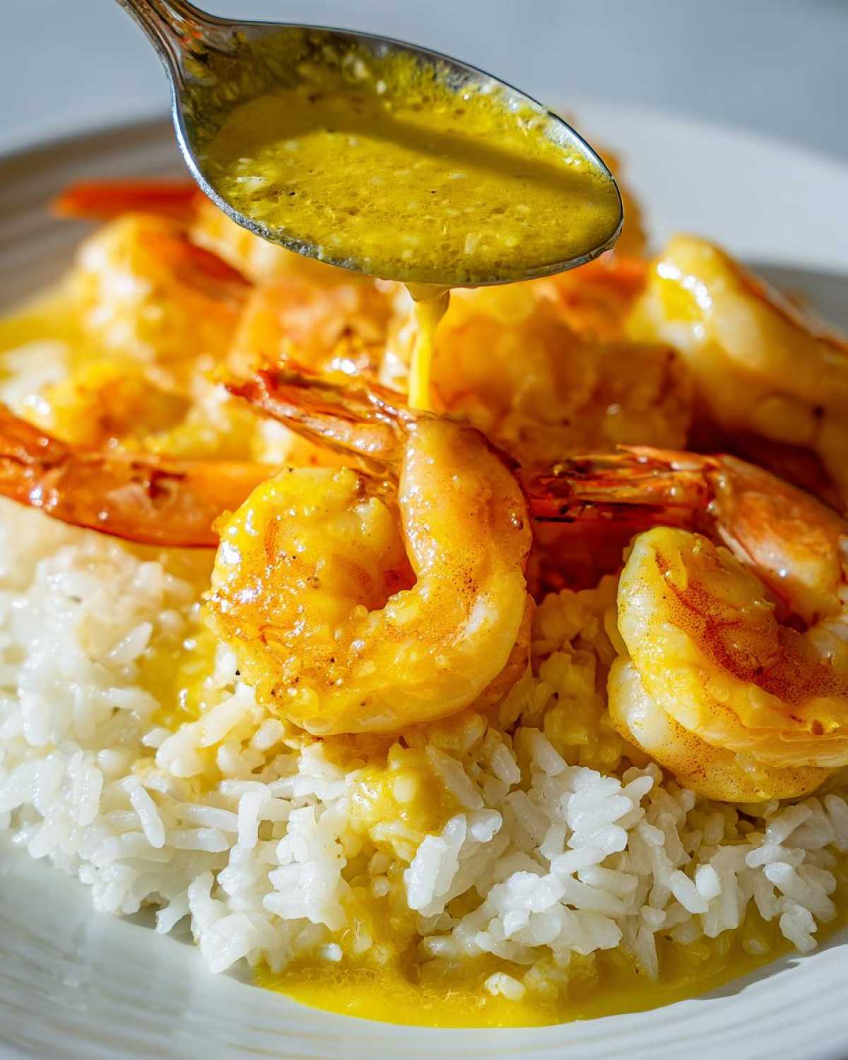 A spoonful of golden garlic butter sauce being poured over cooked shrimp resting on white rice in a Garlic Butter Shrimp and Rice Easy Recipe.
