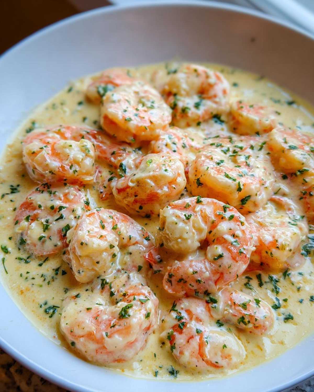 Close-up of plump shrimp coated in a rich, creamy Parmesan sauce, garnished with fresh parsley.
