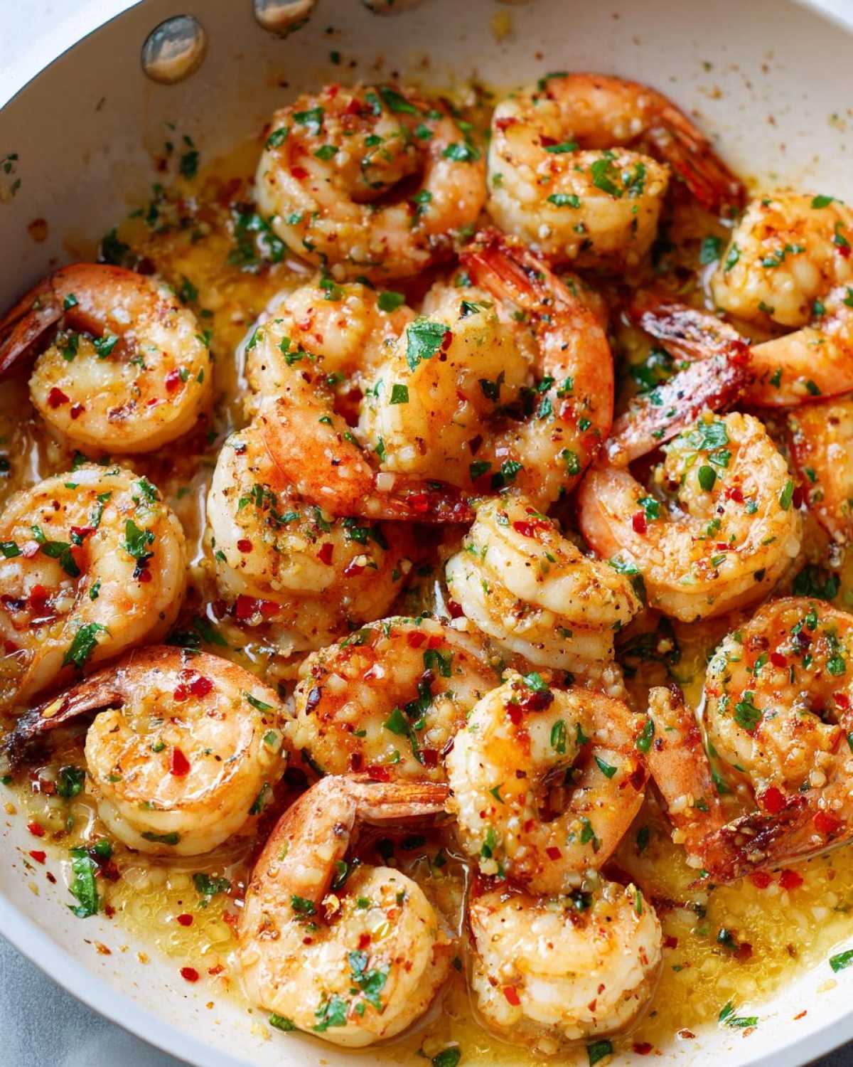 Close-up of succulent shrimp coated in garlic butter sauce, parsley, and red pepper flakes in a skillet.