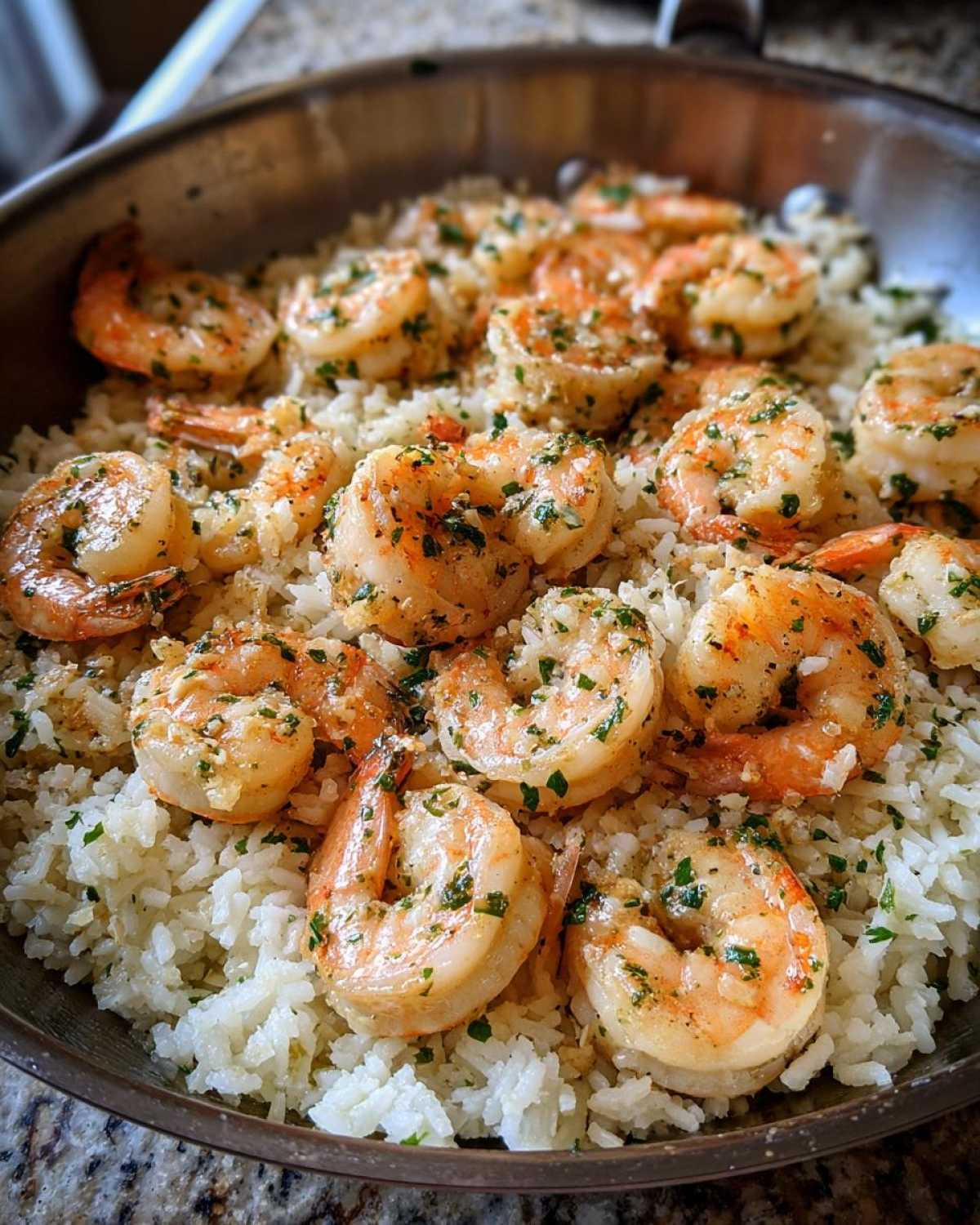 Close-up of cooked shrimp coated in garlic butter and herbs served over white rice in a skillet.