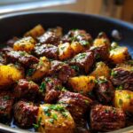 Close-up of seared steak cubes and golden potatoes coated in garlic butter sauce and fresh parsley in a skillet.
