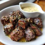 Close-up of tender Garlic Butter Steak Bites coated in garlic and herbs, served with a side of creamy garlic sauce.