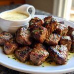 A plate piled high with juicy Garlic Butter Steak Bites, glistening with sauce and parsley, served alongside a small gravy boat of garlic sauce.