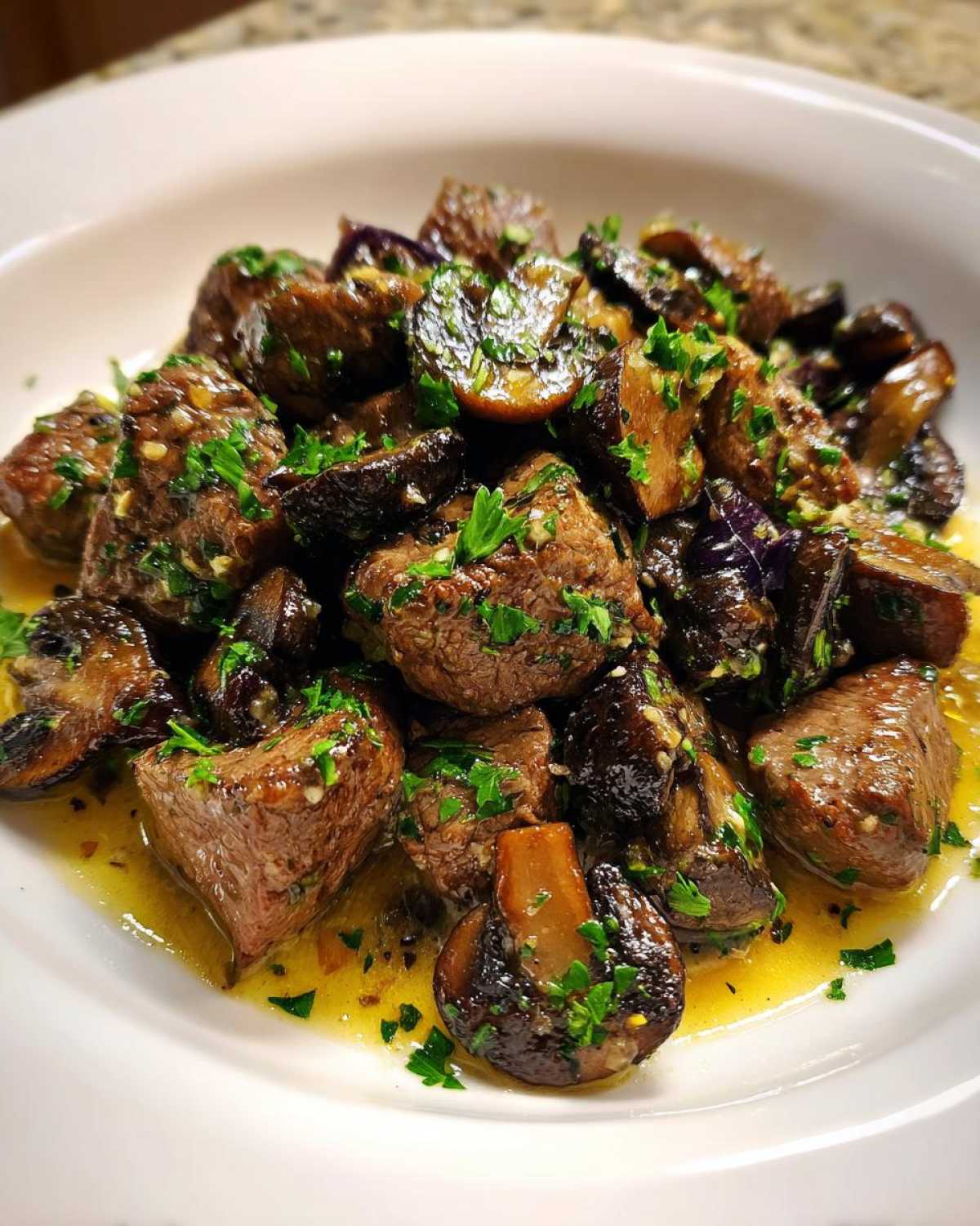 A close-up of juicy Garlic Butter Steak Bites with Mushrooms coated in garlic butter sauce and topped with parsley.