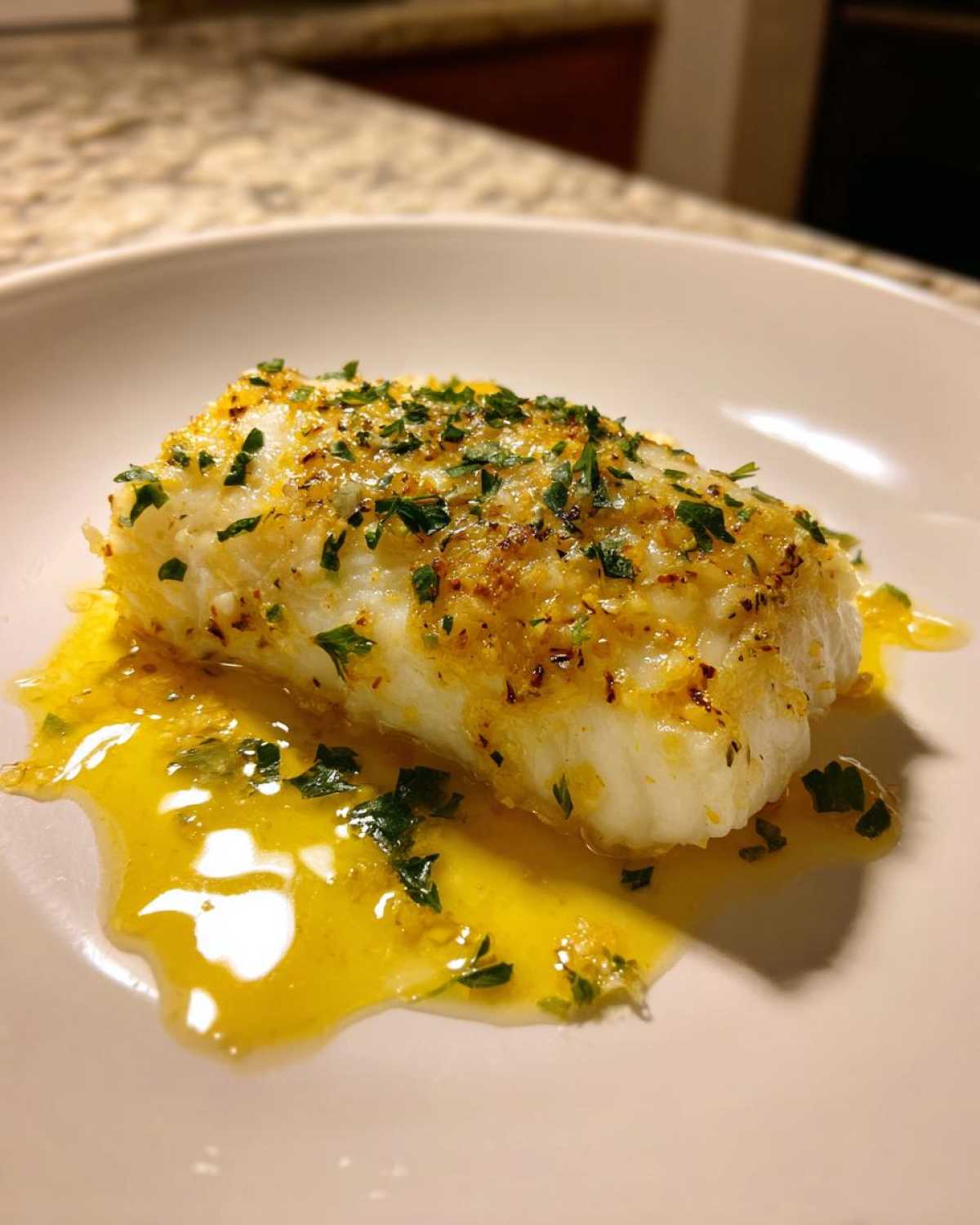 A close-up of a flaky white fillet of Garlic Butter Tilapia with Lemon Sauce, topped with herbs.