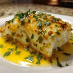 A close-up of a flaky white fillet of Garlic Butter Tilapia with Lemon Sauce, topped with parsley.