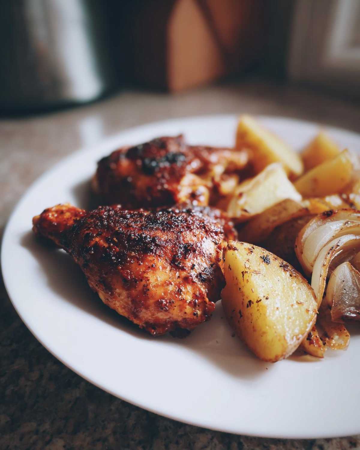 Two pieces of glazed Honey BBQ Chicken Bake served alongside roasted potatoes and onions on a white plate.