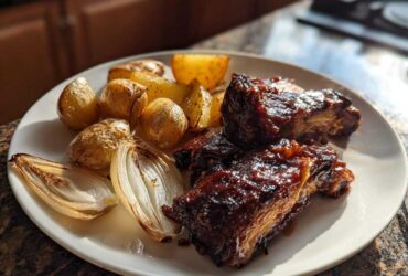 Close-up of Honey BBQ Chicken Bake pieces served with roasted potatoes and caramelized onions on a white plate.