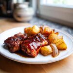 Two pieces of glazed chicken covered in thick Honey BBQ sauce served with roasted potatoes on a white plate.
