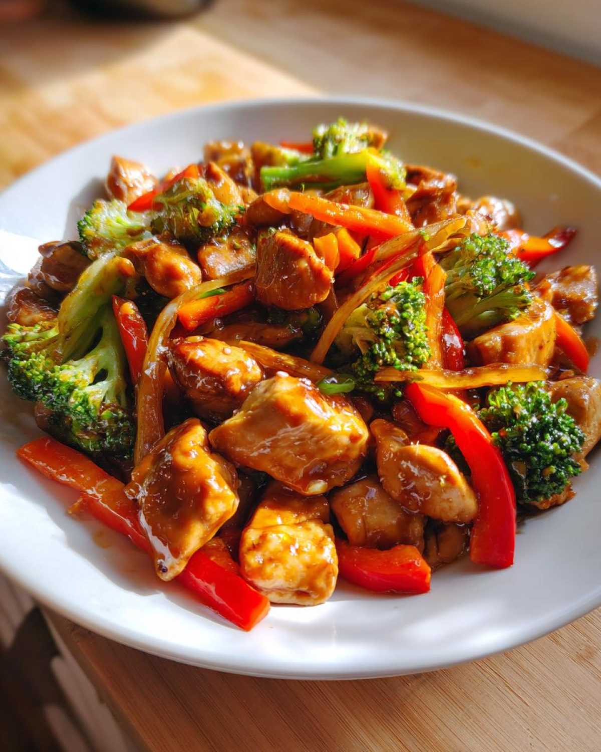 Close-up of glossy Honey Garlic Chicken and Veggie Stir Fry featuring chicken pieces, bright red peppers, and green broccoli florets.