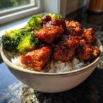 Close-up of a Honey Garlic Chicken Bowl with rice, topped with sticky glazed chicken pieces and bright green steamed broccoli.