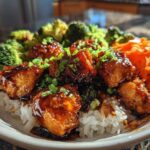 Close-up of a Honey Garlic Chicken Bowl featuring glazed chicken pieces over rice, served with steamed broccoli and shredded carrots.