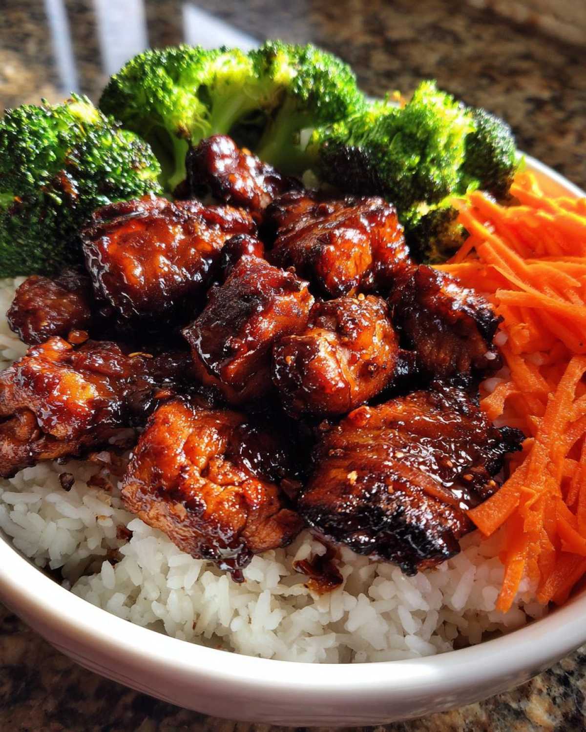 Close-up of a Honey Garlic Chicken Bowl featuring glazed chicken pieces over white rice, fresh broccoli florets, and shredded carrots.