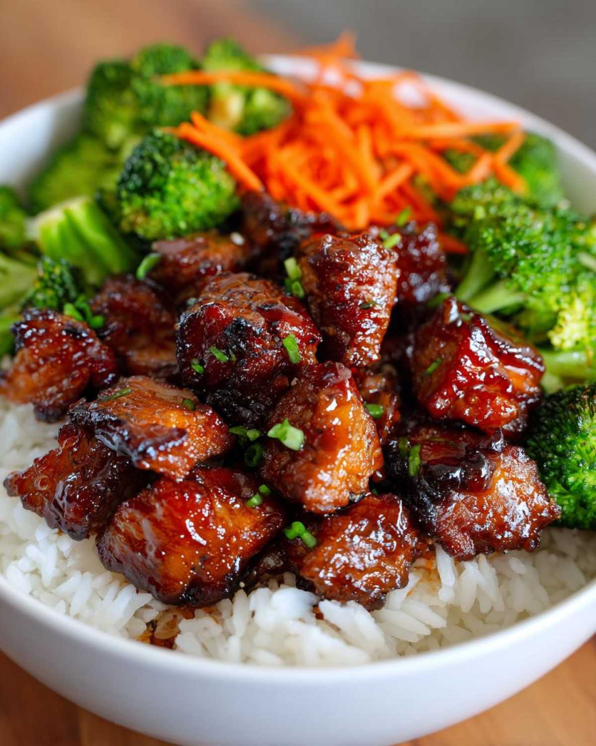 Close-up of a Honey Garlic Chicken Bowl featuring glazed chicken pieces over white rice with steamed broccoli and shredded carrots.