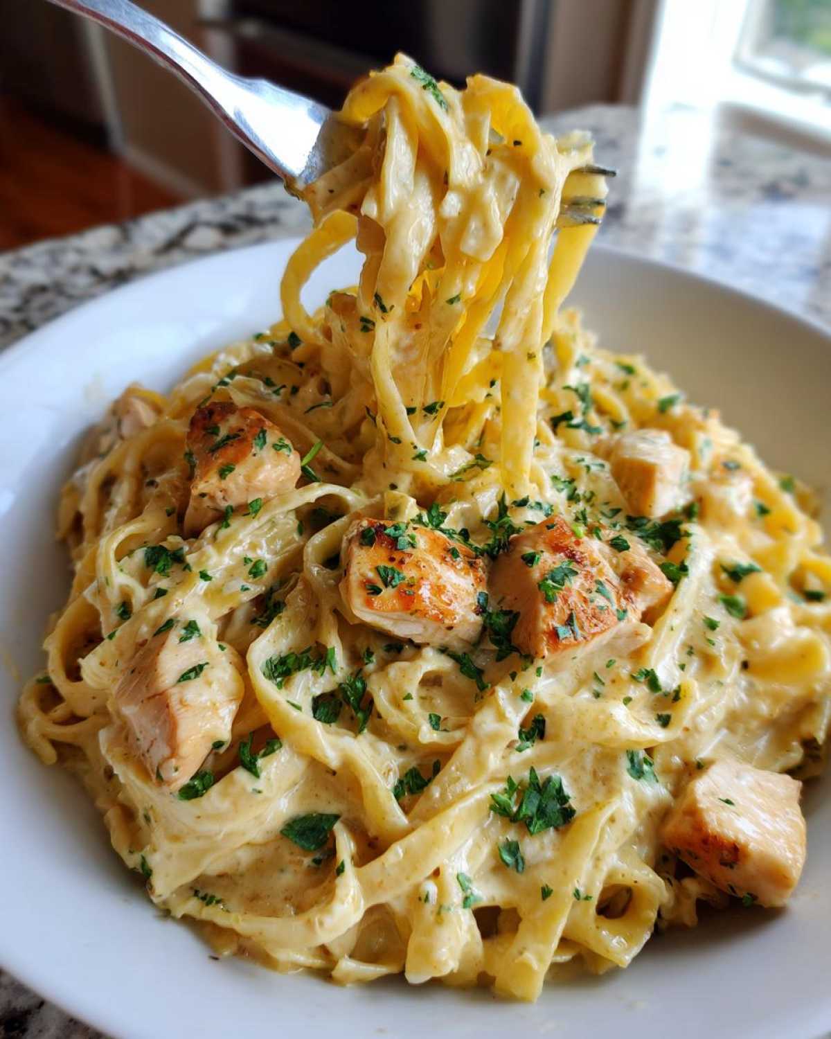 A fork lifting fettuccine noodles coated in cream sauce from a bowl of Honey Garlic Chicken Pasta with diced chicken.