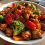 A white bowl filled with glistening Honey Garlic Chicken and Veggie Stir Fry, featuring broccoli, carrots, and red peppers.