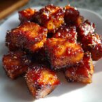 Close-up of shiny, caramelized Honey Garlic Salmon Bites stacked on a white plate, showing dark, sticky edges.