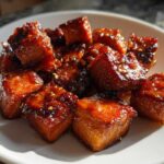Close-up of shiny, caramelized Honey Garlic Salmon Bites sprinkled with sesame seeds on a white plate.