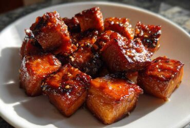 Close-up of shiny, caramelized Honey Garlic Salmon Bites sprinkled with sesame seeds on a white plate.