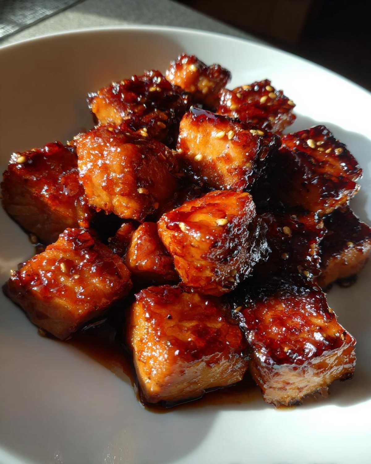 Close-up of glistening Honey Garlic Salmon Bites with caramelized edges and sesame seeds in a white bowl.