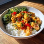 A close-up of a Honey Mustard Chicken Bowl with Rice, featuring saucy chicken pieces, red peppers, and steamed broccoli.