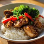 A close-up of a Honey Mustard Chicken Bowl with rice, topped with glazed chicken pieces, bright red bell peppers, and steamed broccoli florets.