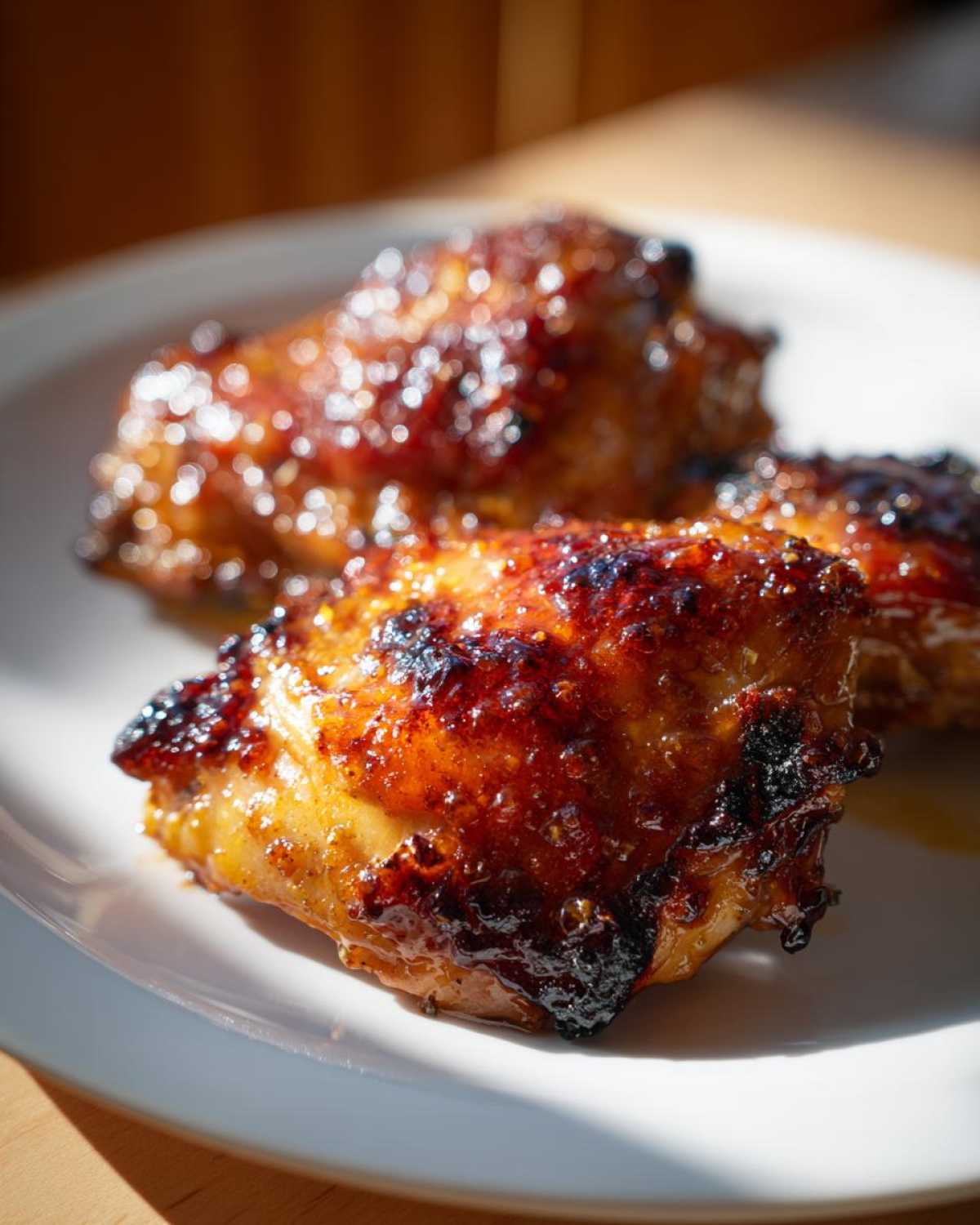 Close-up of perfectly caramelized Honey Mustard Chicken Thighs Oven Roasted with a shiny, dark glaze on a white plate.