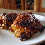 Two pieces of perfectly cooked Honey Mustard Chicken Thighs Oven Roasted with a dark, sticky glaze on a white plate.