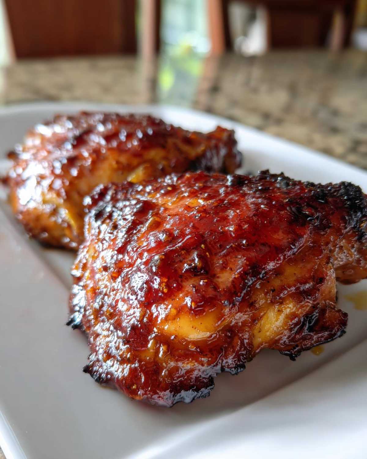 Close-up of two perfectly glazed Honey Mustard Chicken Thighs Oven Roasted on a white plate.