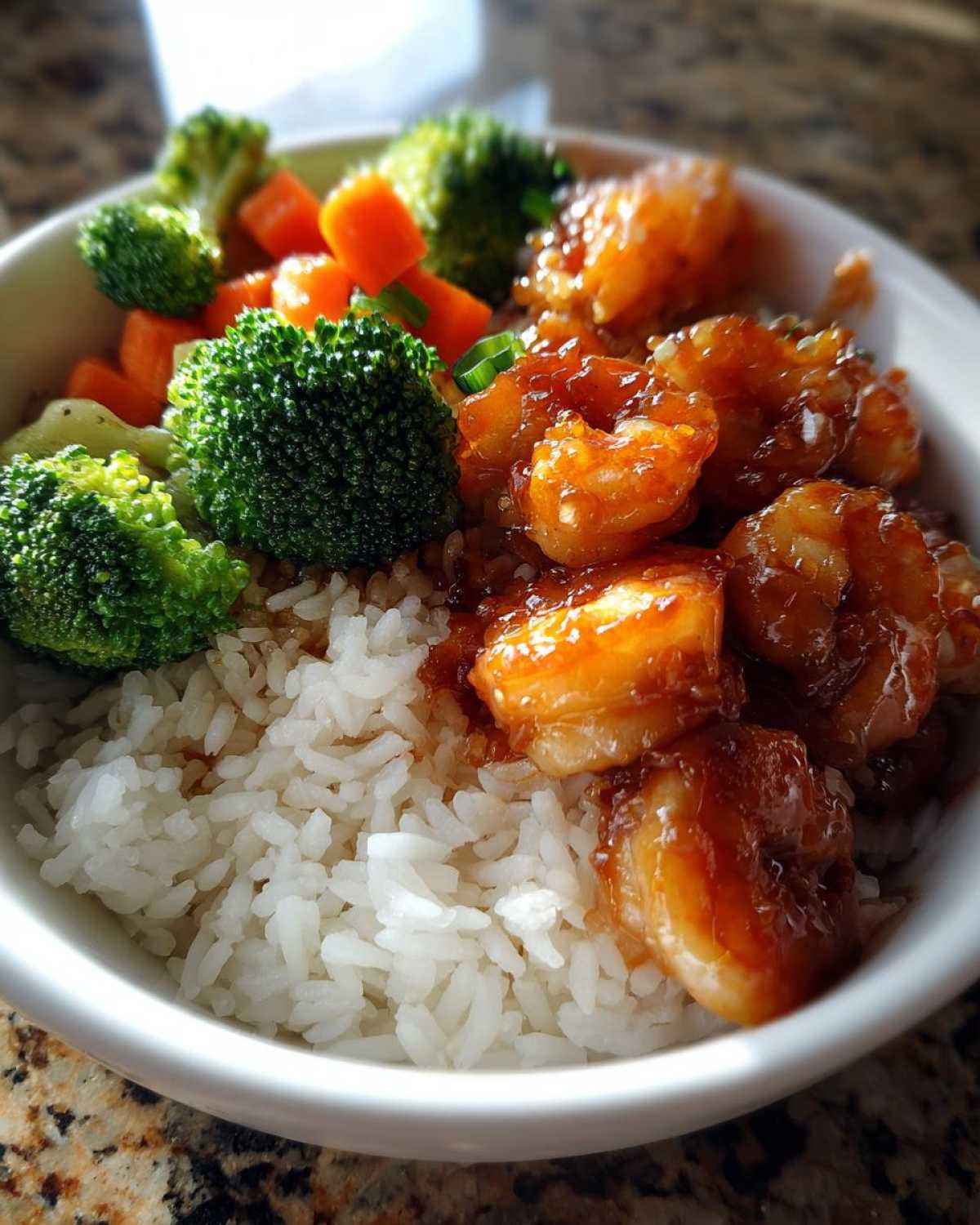 A close-up of a white bowl containing Honey Soy Shrimp Bowl with Rice, steamed broccoli, and carrots.
