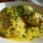 Close-up of tender chicken breasts smothered in a vibrant yellow Lemon Cream Chicken with Fresh Herbs Sauce.