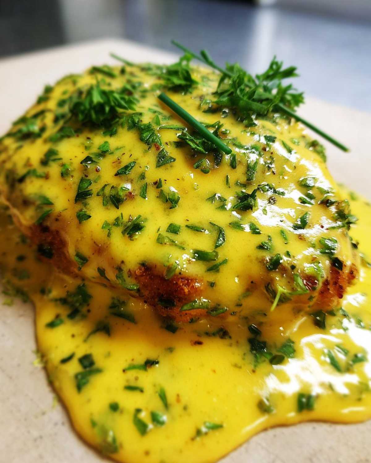 Close-up of a piece of chicken smothered in bright yellow Lemon Cream Chicken with Fresh Herbs Sauce and topped with chopped parsley.