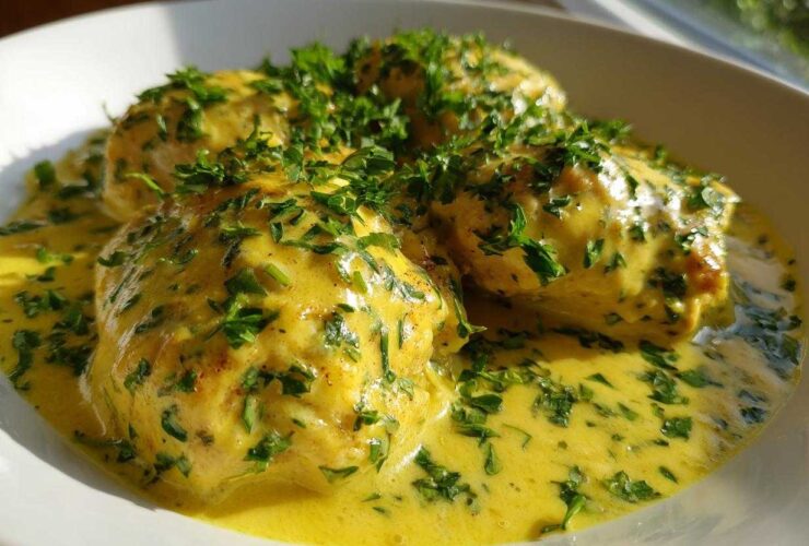 Close-up of tender chicken breasts smothered in a vibrant yellow Lemon Cream Chicken with Fresh Herbs Sauce.