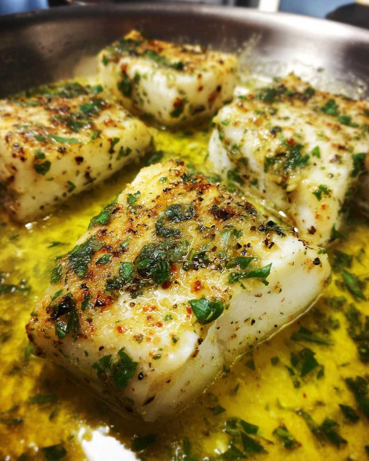 Close-up of chicken pieces cooking in a skillet with bright yellow lemon garlic butter sauce and fresh parsley.