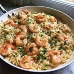 Close-up of a white skillet filled with creamy Lemon Garlic Shrimp Orzo Dinner, topped with fresh parsley.