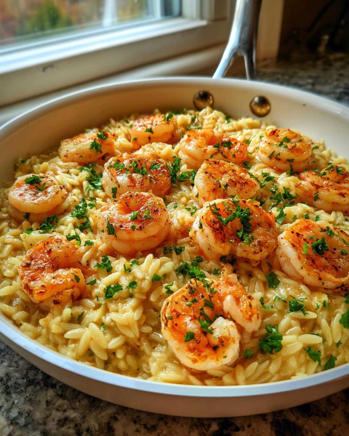 Close-up of a white skillet filled with creamy Lemon Garlic Shrimp Orzo, topped with seared shrimp and fresh parsley.