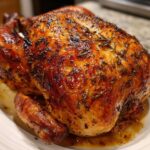 A beautifully browned whole Lemon Herb Roasted Chicken with glossy, crispy skin covered in herbs.
