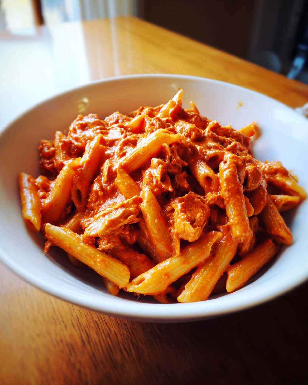 A white bowl filled with One Pot Creamy Tomato Pasta with Chicken, featuring penne pasta coated in a rich, orange-red sauce.