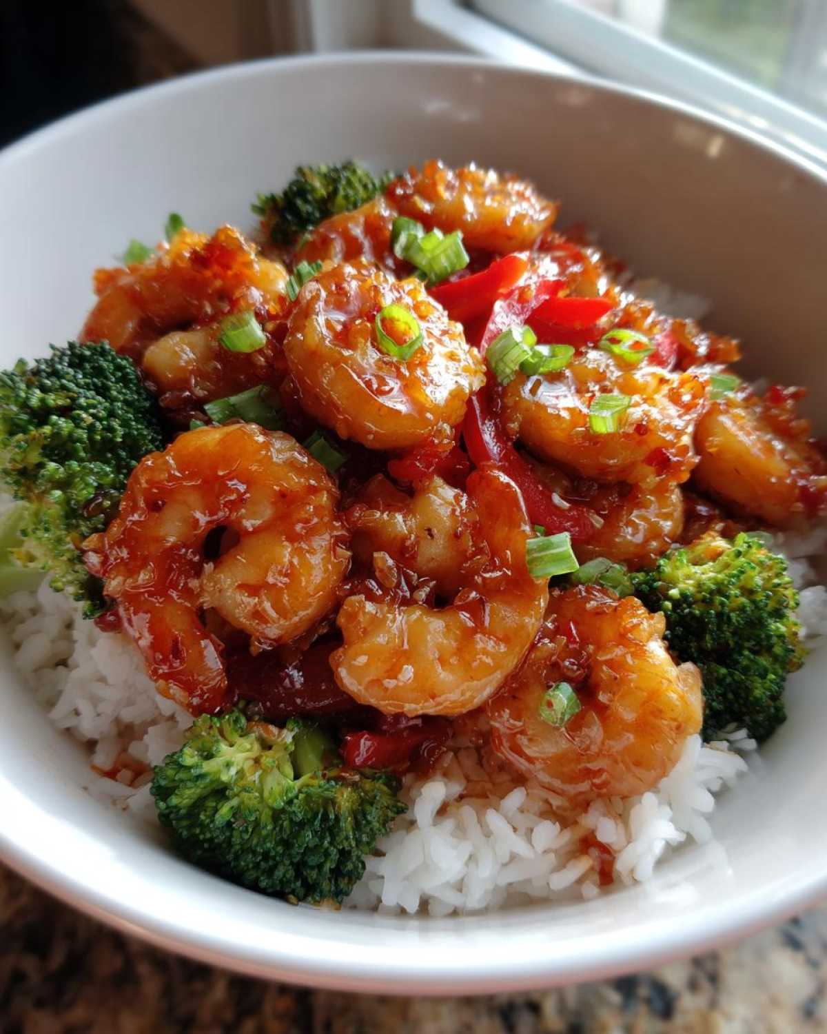 A close-up of a Spicy Honey Garlic Shrimp with Rice Bowl, featuring glazed shrimp, broccoli, and peppers over white rice.