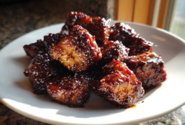 A close-up photo of glistening Sticky BBQ Chicken Bites with caramelized edges piled on a white plate.