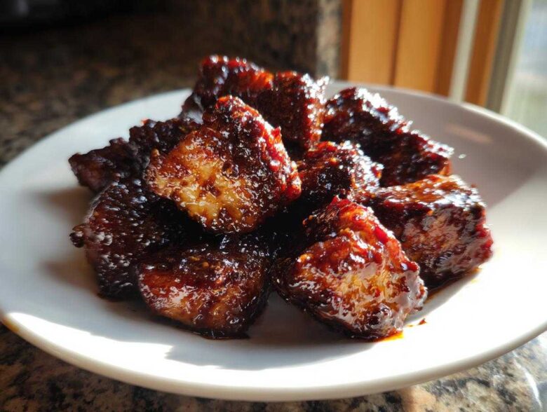 A close-up photo of glistening Sticky BBQ Chicken Bites with caramelized edges piled on a white plate.