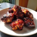 Close-up of several Sticky BBQ Chicken Bites with caramelized edges piled on a white plate.